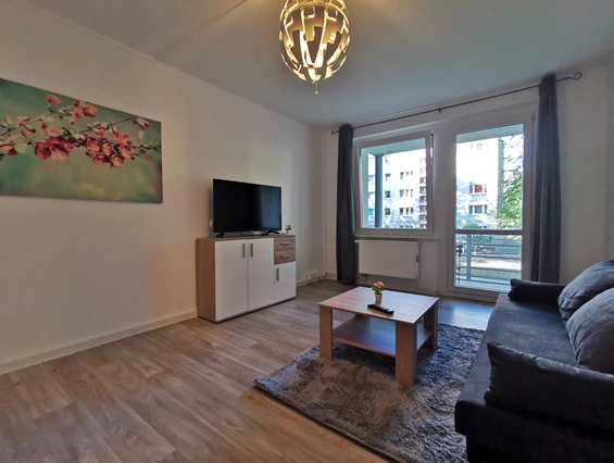 Monteurzimmer: Offener Essbereich im Wohnzimmer mit Couch und Fernseher sowie Zugang zum Balkon. - flex living -  Monteurwohnungen in Freiberg