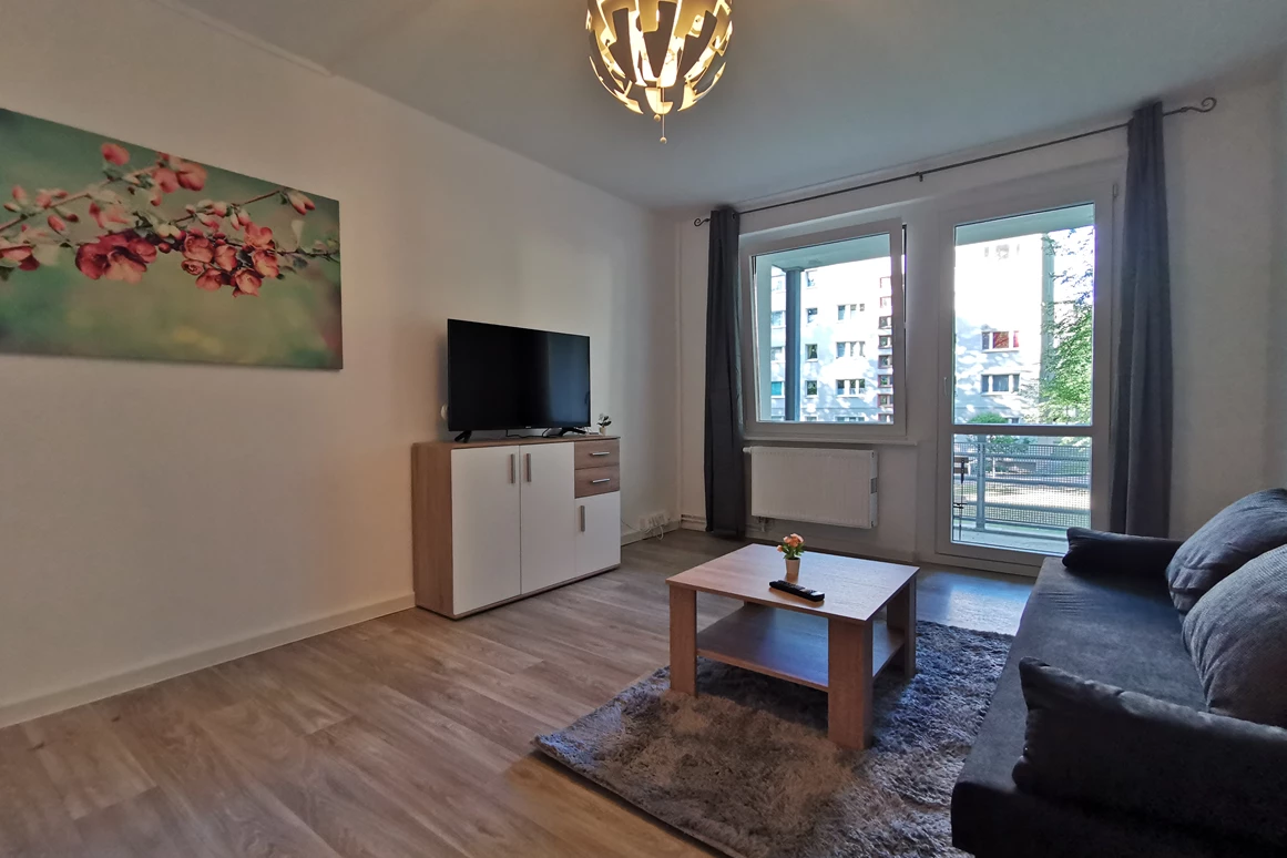 Monteurzimmer: Offener Essbereich im Wohnzimmer mit Couch und Fernseher sowie Zugang zum Balkon. - flex living -  Monteurwohnungen in Freiberg
