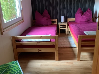 Monteurzimmer: Erstes Schlafzimmer mit zwei Einzelbetten, Nachttisch mit Nachttischlampe, Kleiderschrank, Stuhl, Fernseher und Verdunklungsrollo. - Pension Lausa