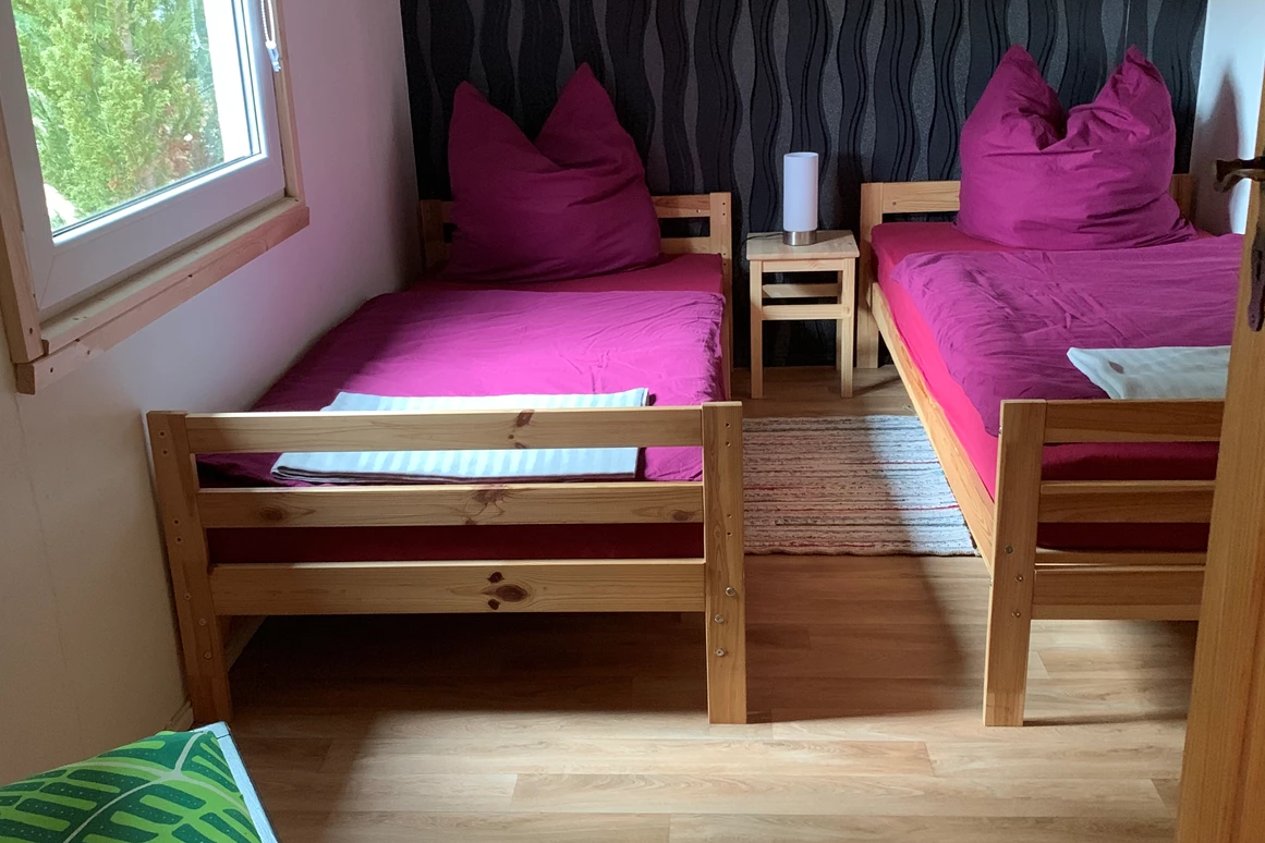 Monteurzimmer: Erstes Schlafzimmer mit zwei Einzelbetten, Nachttisch mit Nachttischlampe, Kleiderschrank, Stuhl, Fernseher und Verdunklungsrollo. - Pension Lausa