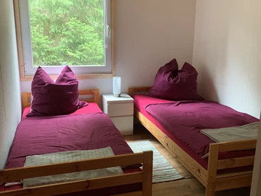 Monteurzimmer: Zweites Schlafzimmer mit zwei Einzelbetten, Nachttisch mit Nachttischlampe, Regal, Stuhl, Fernseher und Verdunklungsrollo. - Pension Lausa