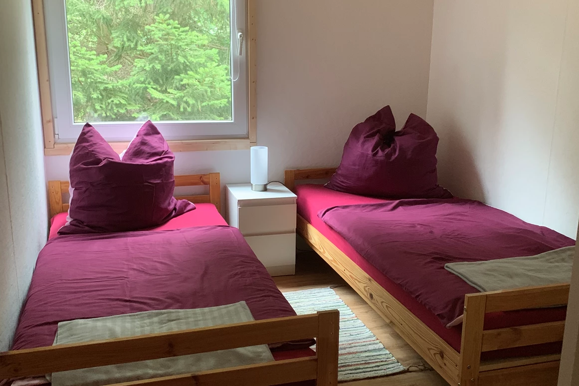 Monteurzimmer: Zweites Schlafzimmer mit zwei Einzelbetten, Nachttisch mit Nachttischlampe, Regal, Stuhl, Fernseher und Verdunklungsrollo. - Pension Lausa