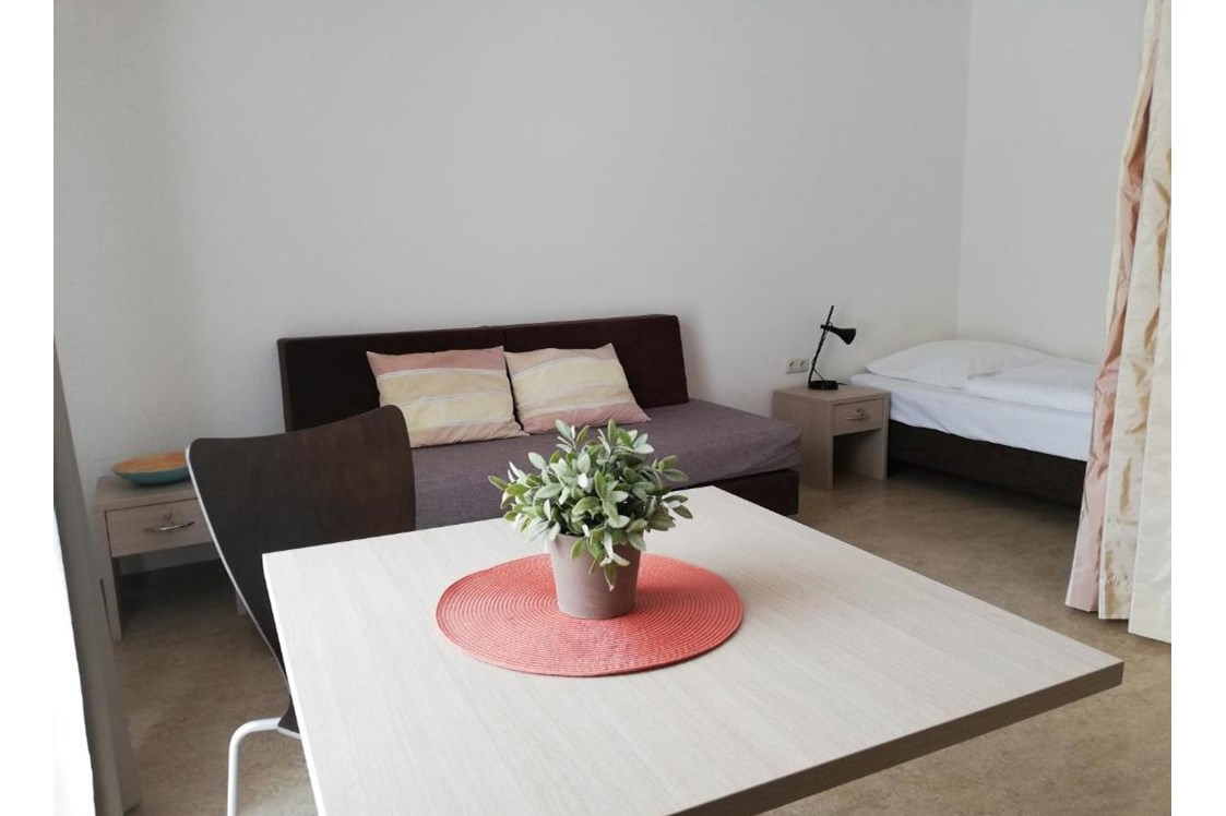 Monteurzimmer: Sitzbereich und Bett im Hintergrund - Berger's Airport Hostel