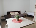 Monteurzimmer: Sitzbereich und Bett im Hintergrund - Berger's Airport Hostel