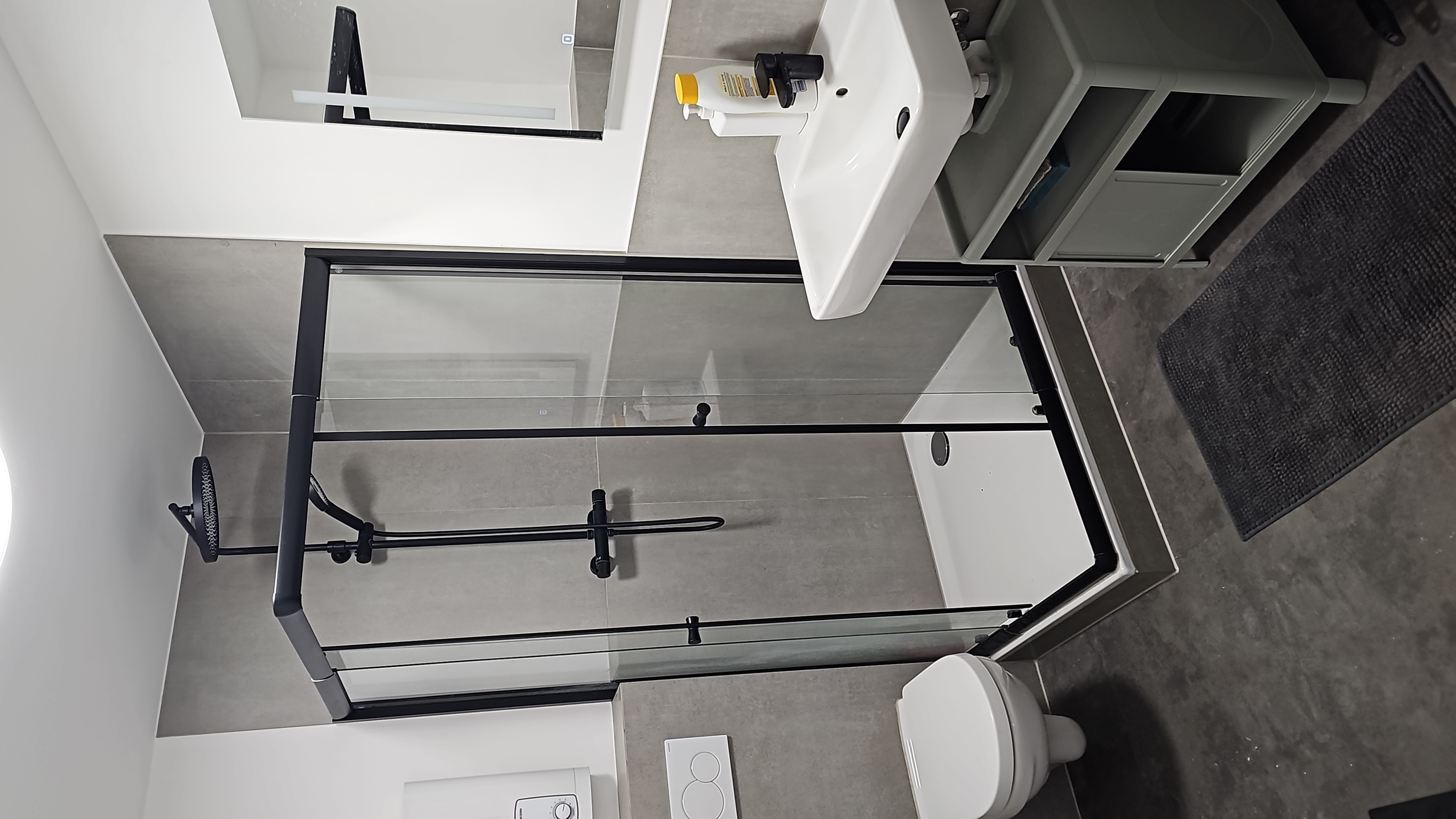Monteurzimmer: Das moderne Badezimmer überzeugt mit einer großzügigen Glasdusche mit Regendusche und 
Handbrause in stilvollem Schwarz-Design, Hänge-WC sowie Waschbecken mit Unterschrank. 
Betonfliesen-Optik verleiht dem Bad ein hochwertiges Erscheinungsbild. - Möblierte Monteurwohnung zur Miete