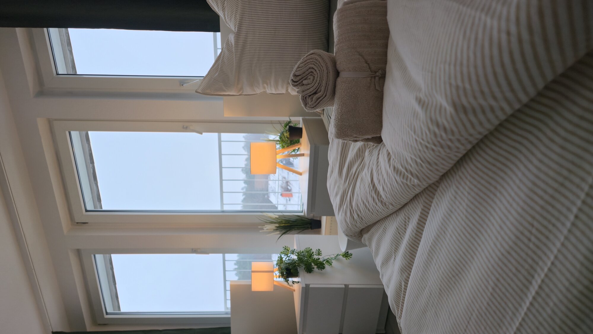 Monteurwohnung - PLZ 60435 (Deutschland) - Bett und Nachttische vor bodentiefen Fenstern - KWATERA24 Monteurwohnung Heusenstamm