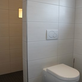 Monteurzimmer: WC, dahinter die Dusche mit beleuchteter Nische zum Abstellen von Pflegemitteln, Seife, Duschgel usw, - Monty